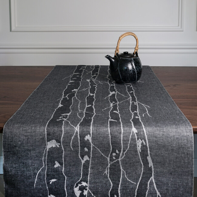 Image of Bjork table runner in black purl side on a dining table from the front with a ceramic coffee pot, from Klassbol&#39;s linen vaveri