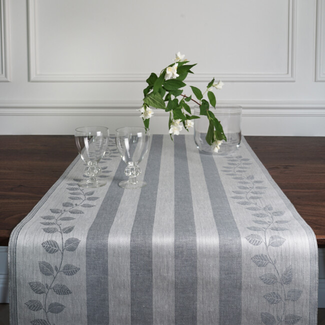 Image of Prunus table runner in the color dimbla, with a white flower in a glass vase uppepa, by Klassbol&#39;s linen vaveri