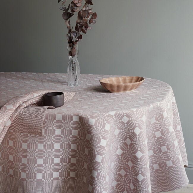 The tablecloth Citron in the color powder pink together with a Citron napkin, a narrow glass vase in the middle of the tablecloth together with dried eucalyptus in a burgundy color - klassbol linen vaveri